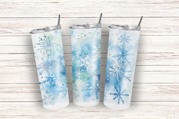 Drei schlanke Thermobecher mit winterlichem Schneeflocken-Design in Blau- und Weißtönen, stehend auf einem hellen Holzuntergrund. Perfekt für heiße oder kalte Getränke mit einem Fassungsvermögen von 590 ml. Ideal für die winterliche Saison und stilvolles